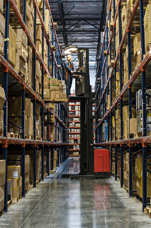 warehouse worker picking order in a reach truck forklift in a narrow aisle