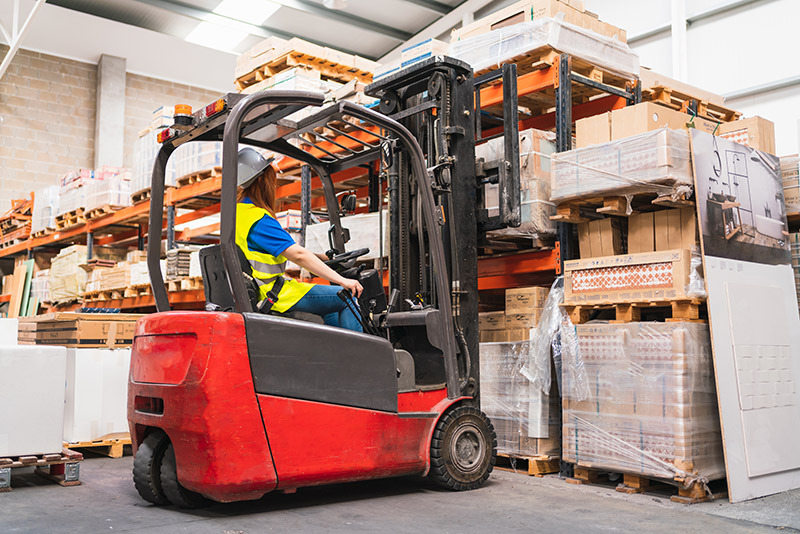 woman picking pallet order with forklift in warehouse